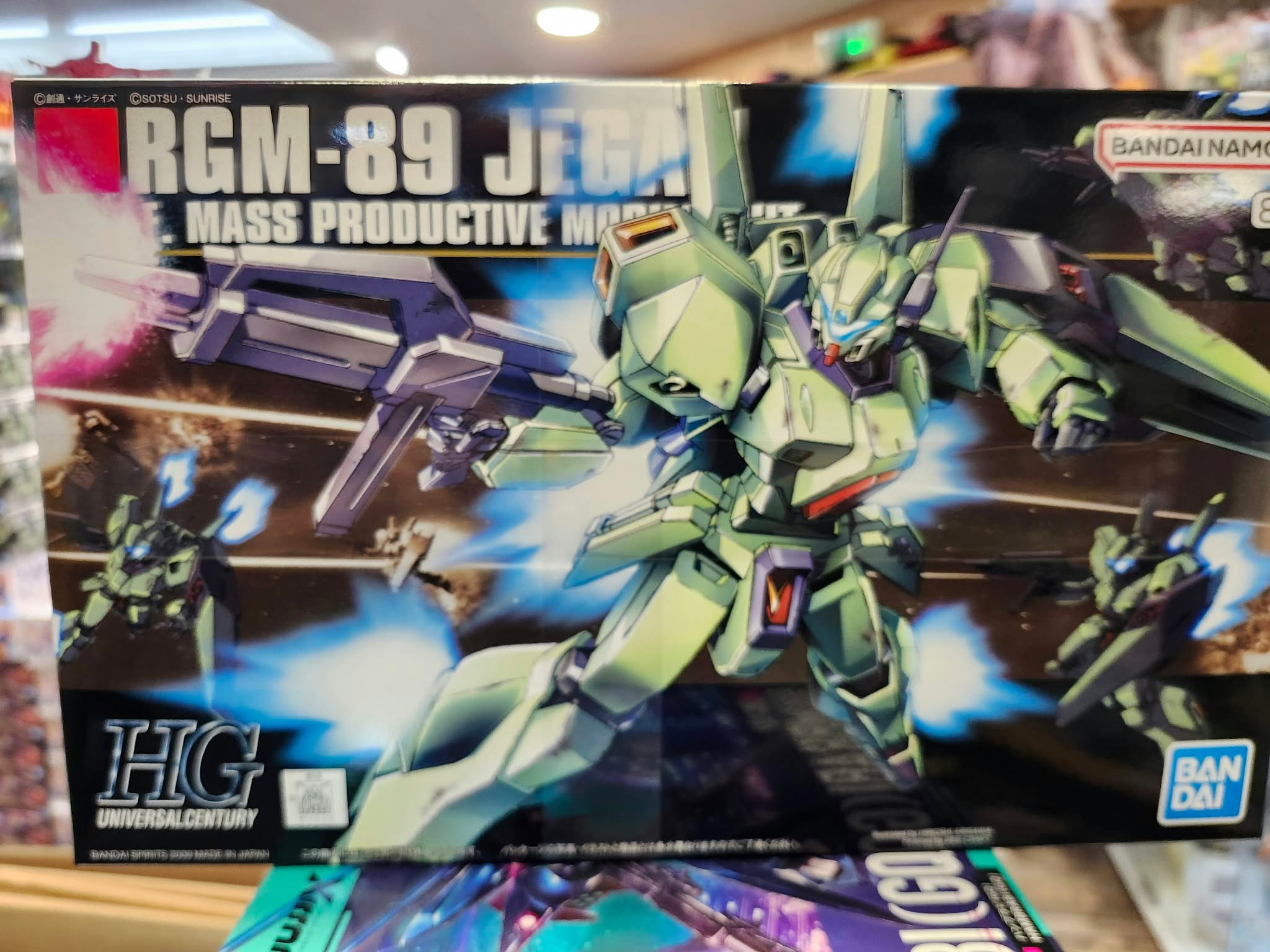 Boîte du HGUC 1/144 RGM-89 Jegan Bandai avec Mobile Suit vert équipé d'un fusil